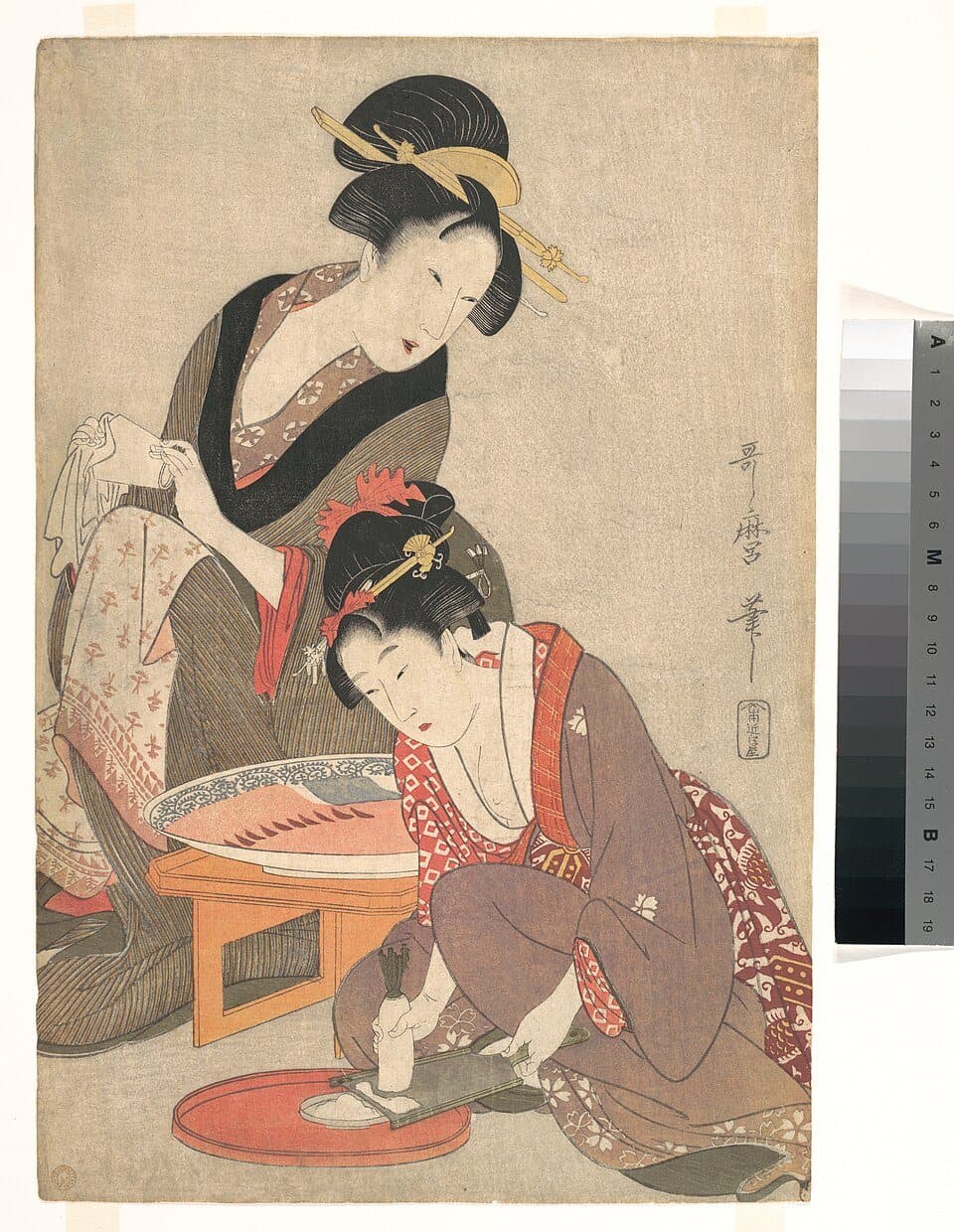 木版画。ひざをついた女性がおろし金で大根をおろし、そばの台に刺身の大皿がある。後ろに布を手にしたもう一人の女性が立つ
