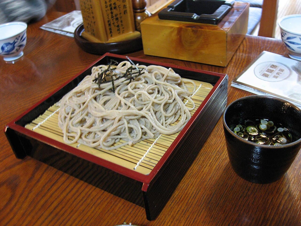 木のテーブルに置かれた、竹のすのこを敷いた朱塗りのせいろのそばと、そばつゆの猪口