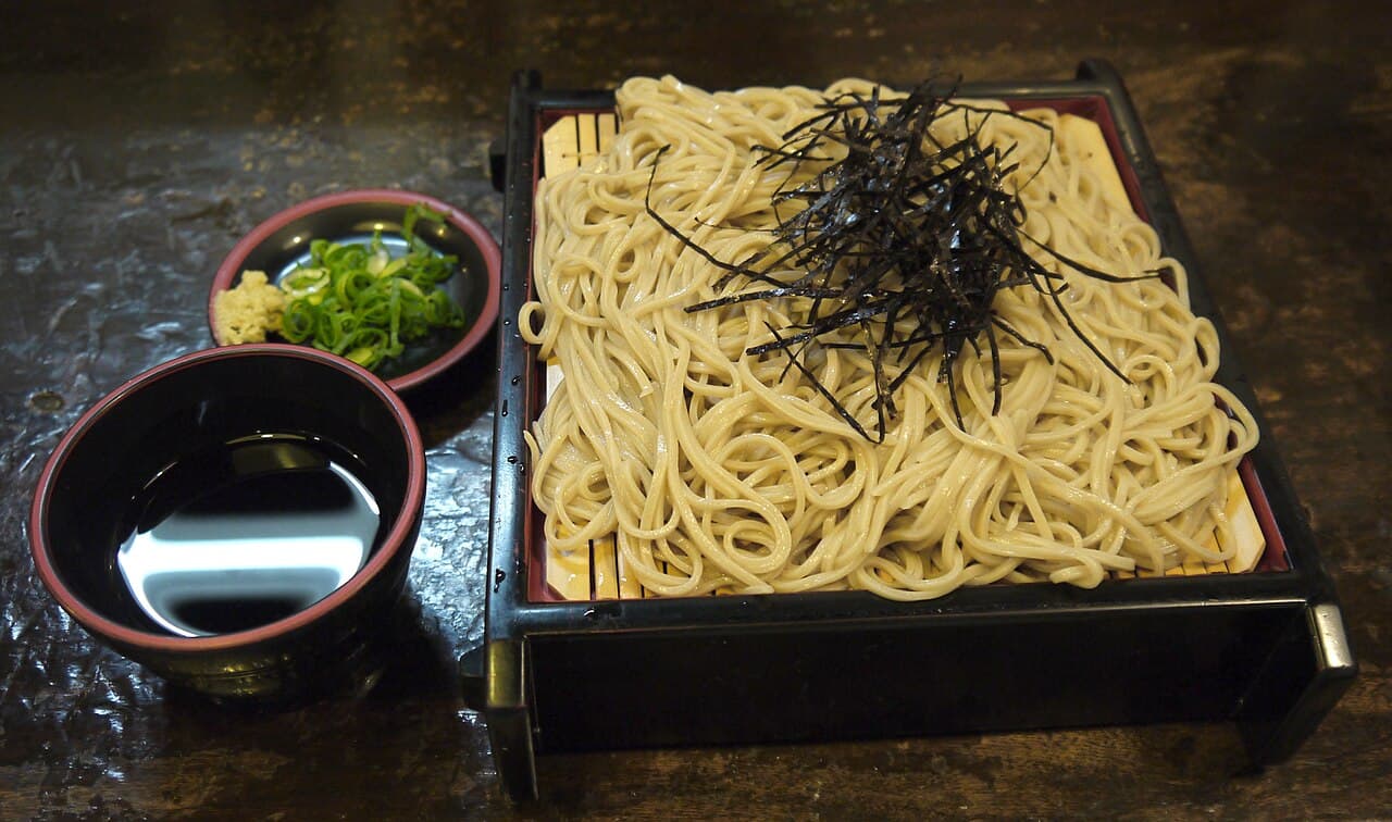 黒い漆塗りのせいろに盛られたざるそば。上に刻み海苔がのり、横にそばつゆの猪口と、ねぎとわさびの小皿が添えられている