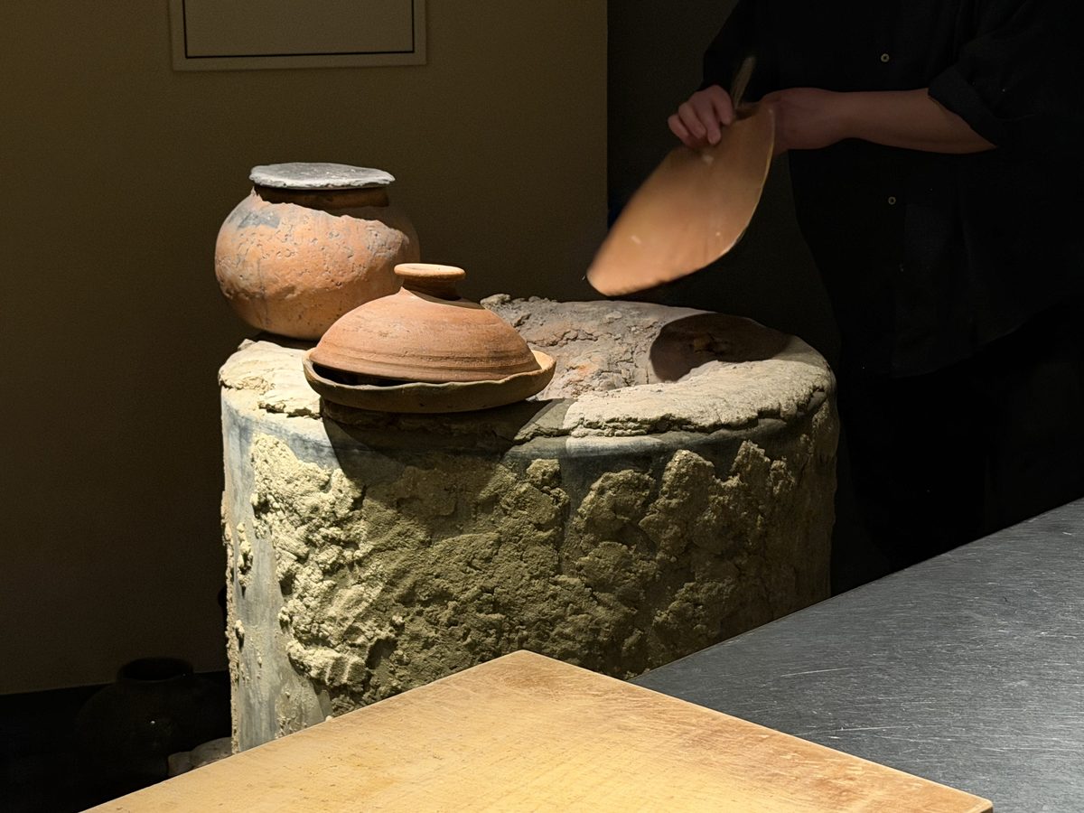 The chef lifting a clay pot lid.