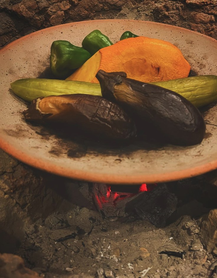Seasonal vegetables on a clay plate over glowing charcoal.